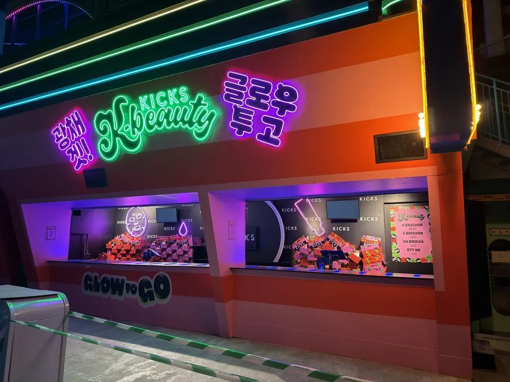 Kicks K-beauty-kiosk på Gröna Lund med fasaden folierad i orange och rosa ränder, neonskyltar i grönt och lila och dekoren ”Glow to go”.