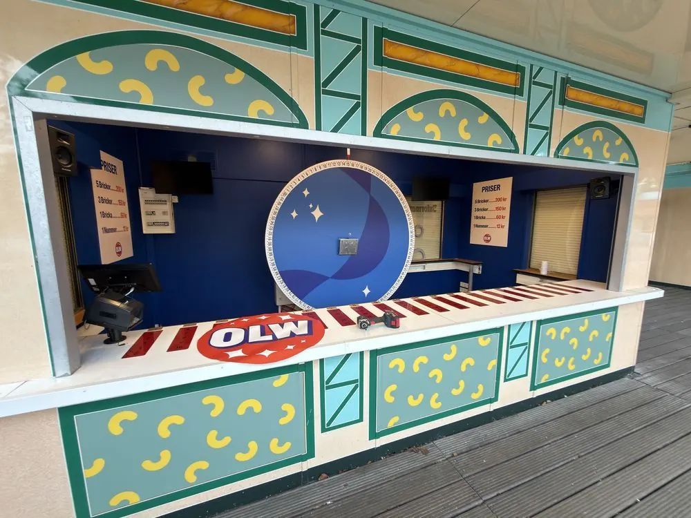 OLW:s spelkiosk på Skara Sommarland med panelerna folierade med ostbågar, OLW-loggan på disken och ett lyckohjul i mitten.